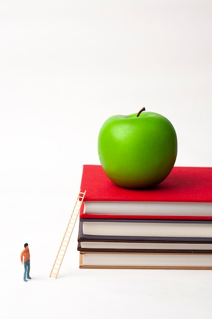 Foto uomo in miniatura in piedi e mela sulla pila di libri nuovi