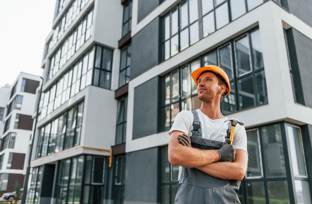 近代的な建物の近くに立って昼間建設で制服を着て働く若い男