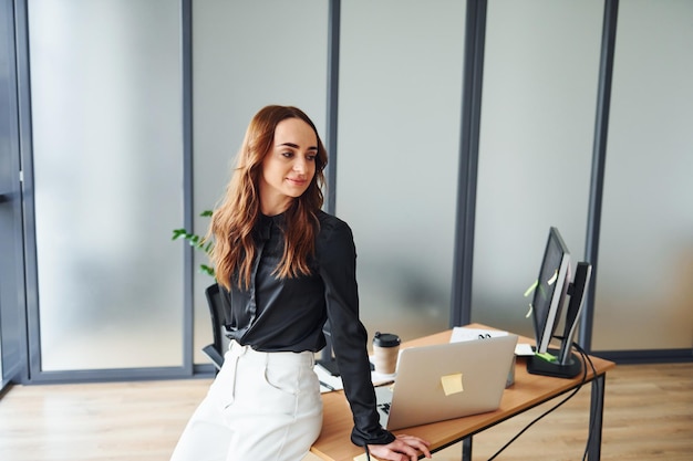 テーブルの近くに立っているフォーマルな服を着た若い大人の女性がオフィスの屋内にいます