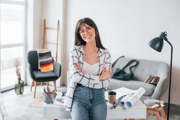 Standing near table Young female freelance worker is indoors in home at daytime