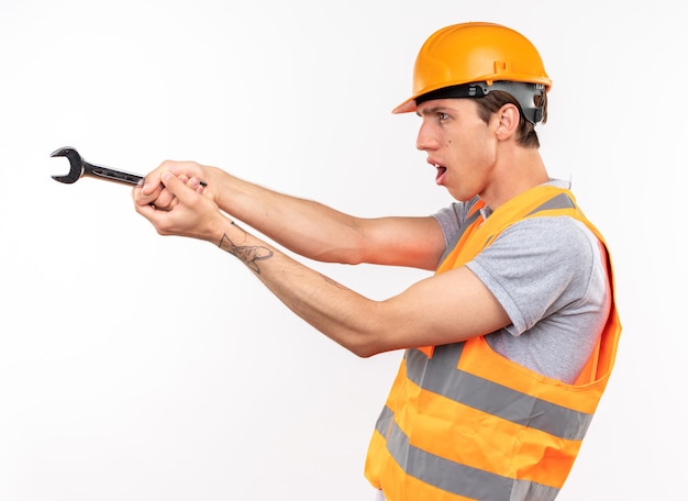 Standing in profile view young builder man in uniform holding out open-end wrench at side