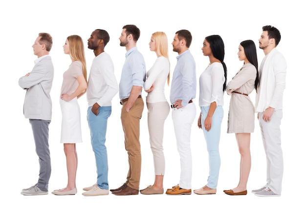 Standing in a row. Full length of confident multi-ethnic group of people in smart casual wear looking away while standing in a row and against white background