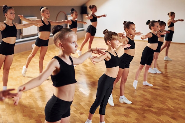 Standing in the row Group of female kids practicing athletic exercises together indoors