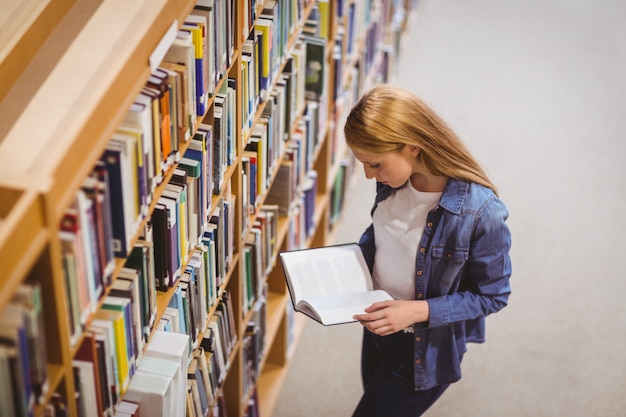 Standing student reading book in library