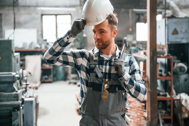 Standing in the warehouse with artificial lighting Factory male worker in uniform is indoors