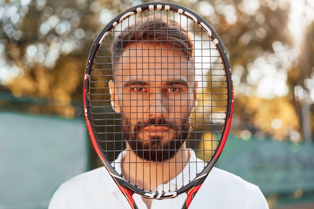 Photo standing with racket in hands young man is on the tennis court at sunny daytime