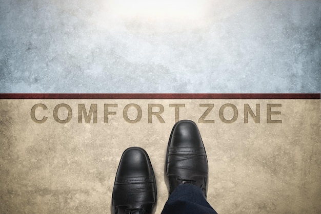Stap uit je comfortzone Comfort Zone Concept Man met leren schoenen Stap over een woord met lijn op betonnen vloer Bovenaanzicht