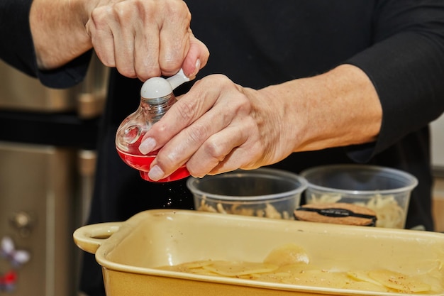 Stap voor stap aardappelgratin recept Handen peper Aardappelschijfjes in glazen ovenschaal Aardappelschotel