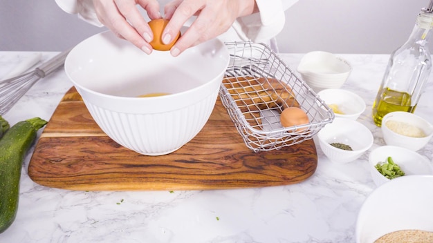 Stap voor stap. Biologische bruine eieren breken in de kom om courgettecakes te maken.