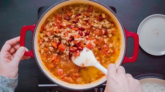 Stap voor stap. Bovenaanzicht. Roeren van kalkoen chili in geëmailleerde gietijzeren overdekte Nederlandse oven.