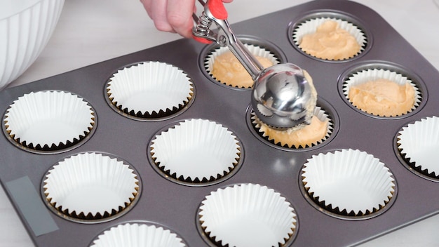 Stap voor stap. Cupcakebeslag in cupcakevormpjes scheppen om vanillecupcakes te bakken.