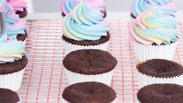 Stap voor stap. Glanzende eenhoorn-chocolade-cupcakes met regenboogkleurige buttercream frosting.