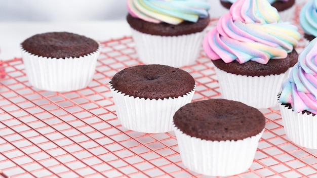 Stap voor stap. Glanzende eenhoorn-chocolade-cupcakes met regenboogkleurige buttercream frosting.