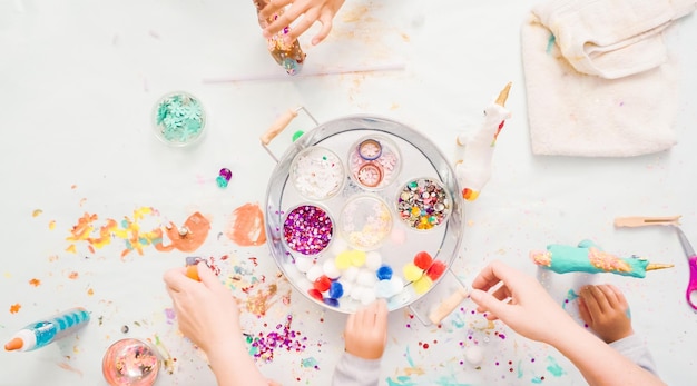 Stap voor stap. Kleine meisjes versieren eenhoorn van papier-maché met glitter en papieren bloemen.