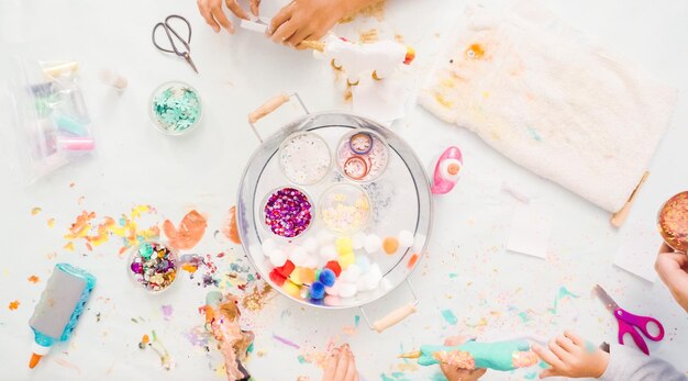 Stap voor stap. Kleine meisjes versieren eenhoorn van papier-maché met glitter en papieren bloemen.