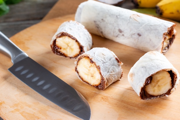 Stap voor stap koken heerlijk broodje met plakjes banaan op houten tafel. bananenrol met chocoladedessert