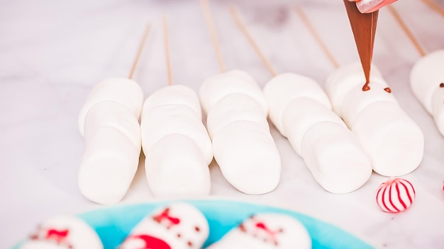 Stap voor stap. Marshmallow-sneeuwman en rendieren maken op stokjes warme chocolademelk toppers voor het geven van voedsel.