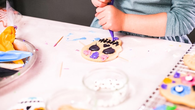 Stap voor stap. Meisje versiert suikerschedelkoekjes met royal icing voor Dia de los Muertos-vakantie.