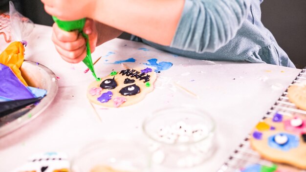 Stap voor stap. Meisje versiert suikerschedelkoekjes met royal icing voor Dia de los Muertos-vakantie.