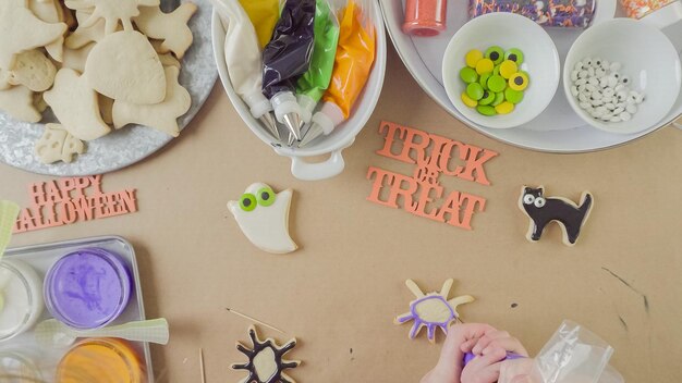 Stap voor stap. Moeder en dochter versieren Halloween-suikerkoekjes met kleurrijke royal icing.