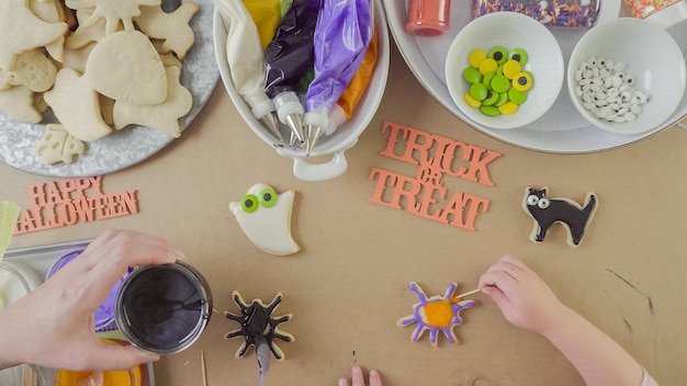 Stap voor stap. Moeder en dochter versieren Halloween-suikerkoekjes met kleurrijke royal icing.