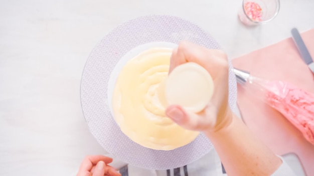 Stap voor stap. Plat leggen. Druppel een witte chocolade ganache op een verjaardagstaart met witte botercrème glazuur.