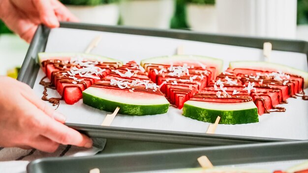 Stap voor stap. Watermeloenpartjes gegarneerd met chocolade en zeezout op het stokje op bakplaat.