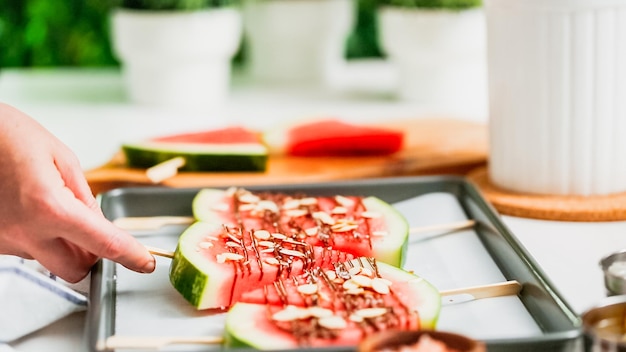 Stap voor stap. Watermeloenpartjes gegarneerd met chocolade en zeezout op het stokje op bakplaat.