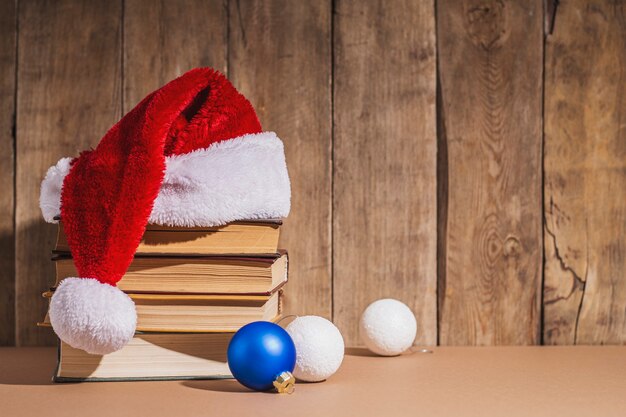 Stapel boeken, kerstboomversieringen en kerstmanhoed op houten ondergrond.