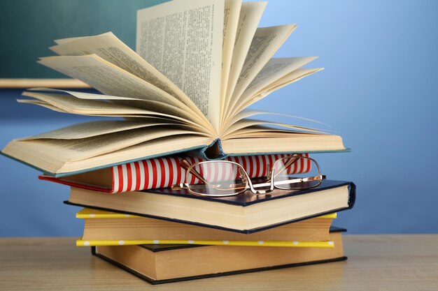 Foto stapel boeken met bril op houten bureau op kleurrijke muur en schoolbord achtergrond