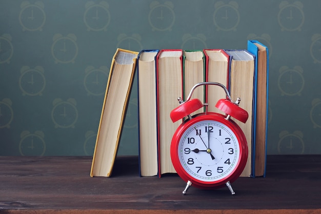 Stapel boeken met kleurendekking en rode retro wekker op de lijst. Terug naar school.