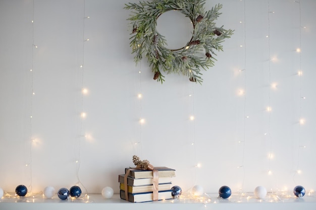 Stapel boeken met lint kerstballen Kerstkrans en kerstverlichting in de buurt van witte muur