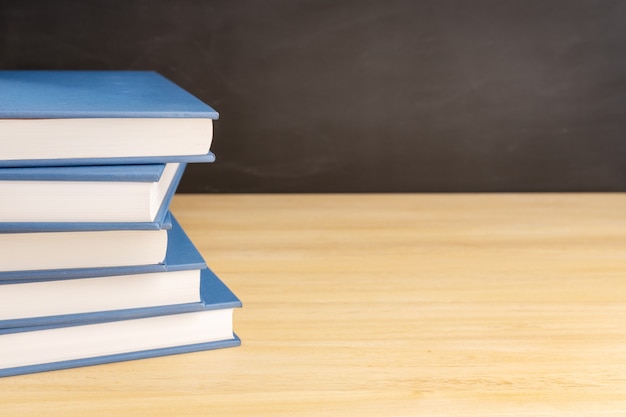 Stapel boeken op houten tafel en zwart bord op de achtergrond met kopieerruimte