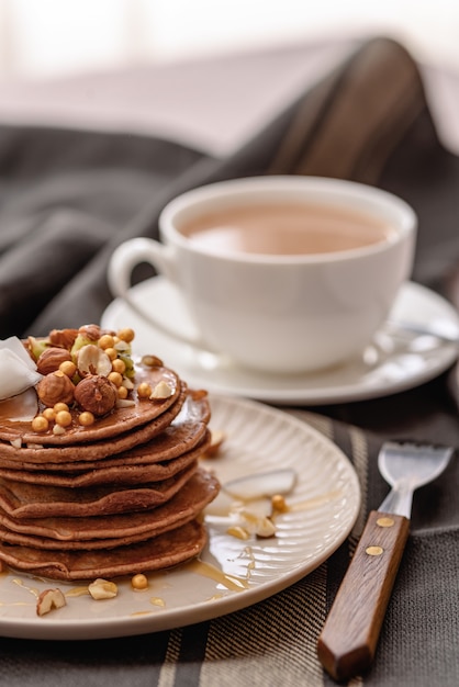 Stapel chocolade pannenkoeken met ahornsiroop, honing en kopje koffie, lekkere snack, verticaal