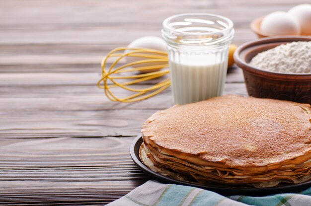 Stapel Franse pannenkoeken in koekenpan op houten keukentafel met melkeieren en bloem opzij