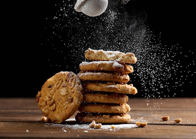 Stapel gebakken ronde koekjes bestrooid met poedersuiker op een houten tafel, zwarte achtergrond