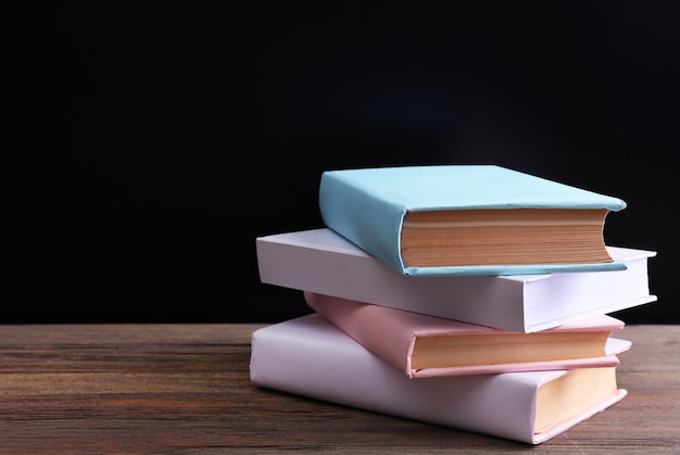 Stapel gesloten kleurrijke boeken op houten tafel tegen zwarte achtergrond