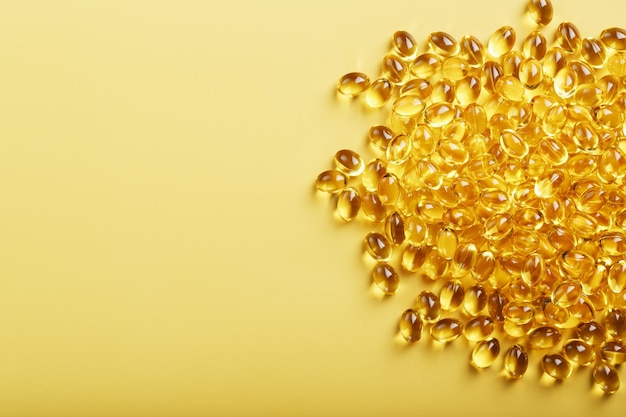 Stapel gouden capsules vitamine D3 op een gele achtergrond met vrije ruimte
