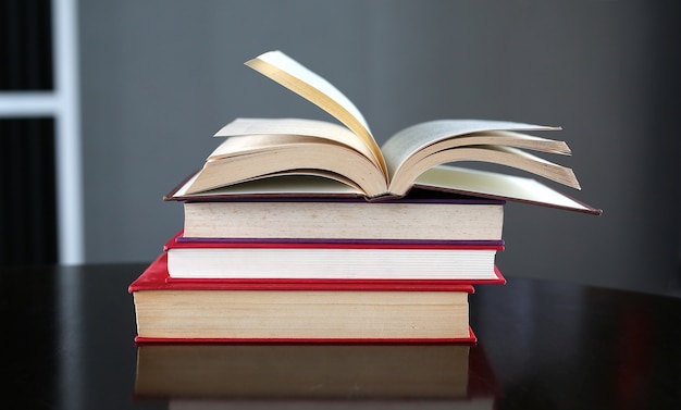 Stapel handboeken op bureau met open boek op de bovenkant in bibliotheekruimte, ba van het Onderwijsconcept