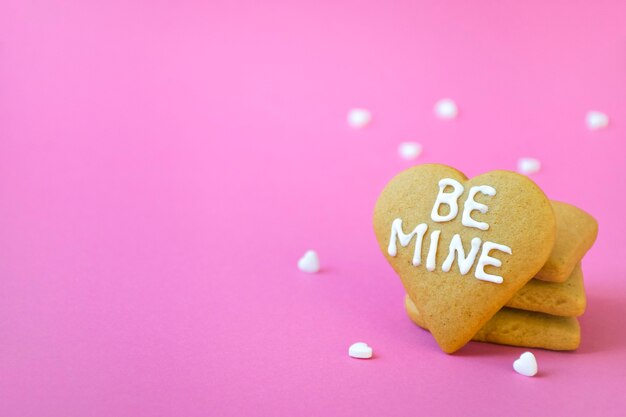 Stapel handgemaakte hartvormige koekjes met de woorden BE MINE en veel witte snoepconfetti. Valentijnsdag, romantiek en liefde