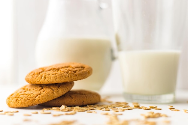 Stapel havermoutkoekjes en havergranenvlokken op witte tafel op melkglaskruikachtergrond