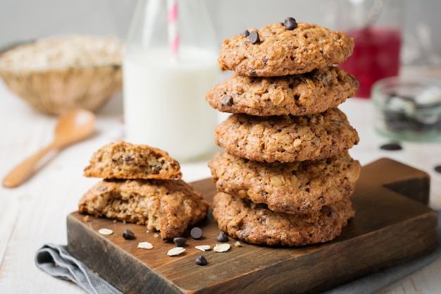 Stapel havermoutkoekjes met chocolade op een licht met vlokken en een fles melk.