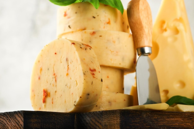 Foto stapel kaas met tomaten en kruiden en zwitserse kaas op met basilicum en mes op serveerplank op lichtgrijze tafelachtergrond assortiment van verschillende kaassoorten kaasachtergrond