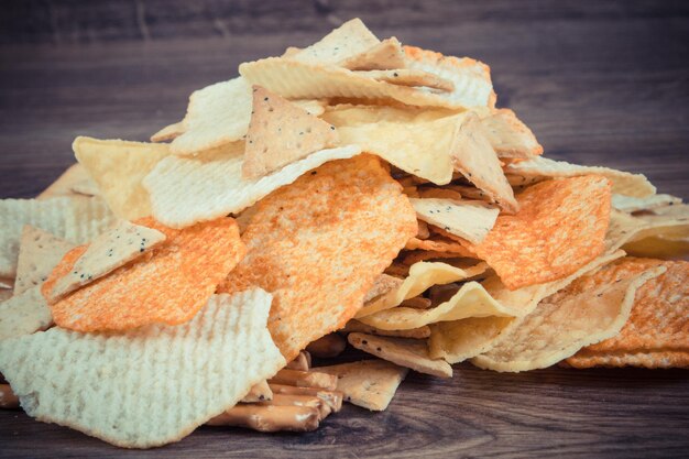 Stapel knapperige gezouten aardappel chips broodstokjes en koekjes op een rustiek bord concept van beperking het eten van ongezond en gezouten voedsel