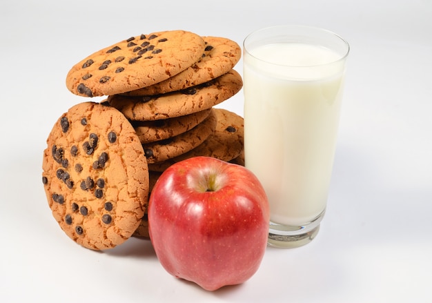 Stapel koekjes met chocolade, glas yoghurt, rode appel op een witte tafel