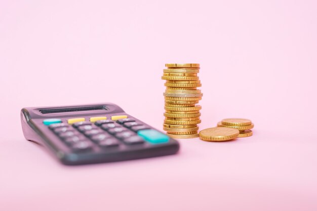 Stapel munten en rekenmachine op een roze achtergrond. Euromunten
