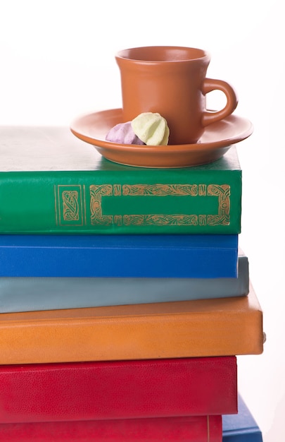 Stapel oude boeken en een kopje koffie op wit wordt geïsoleerd