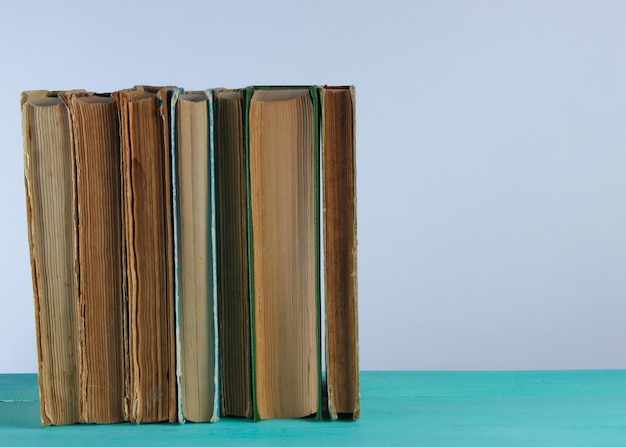 Stapel oude boeken op een plank tegen een witte muur