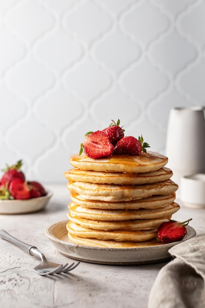 Stapel pannenkoeken met honing, aardbeien en vork zelfgemaakt ontbijtconcept