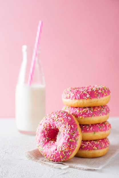 Stapel roze en witte donuts met een fles melk over roze